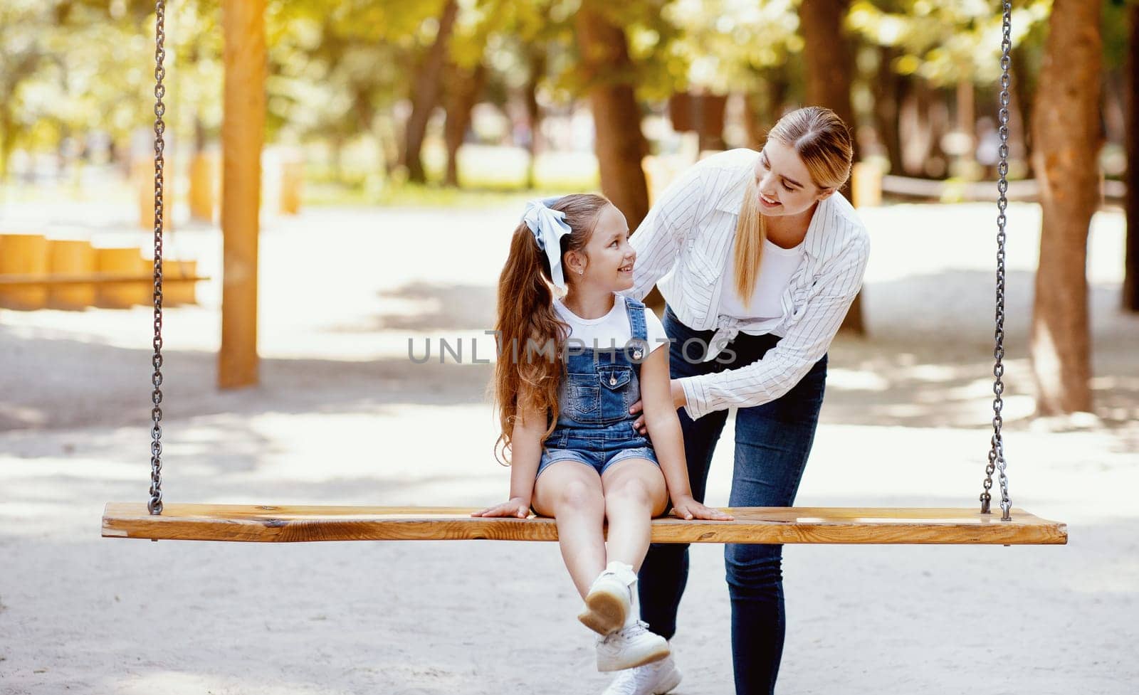 Mother Pushing Little Daughter On The Swings Spending Time Together On Playground In Park Outside. Weekend Concept