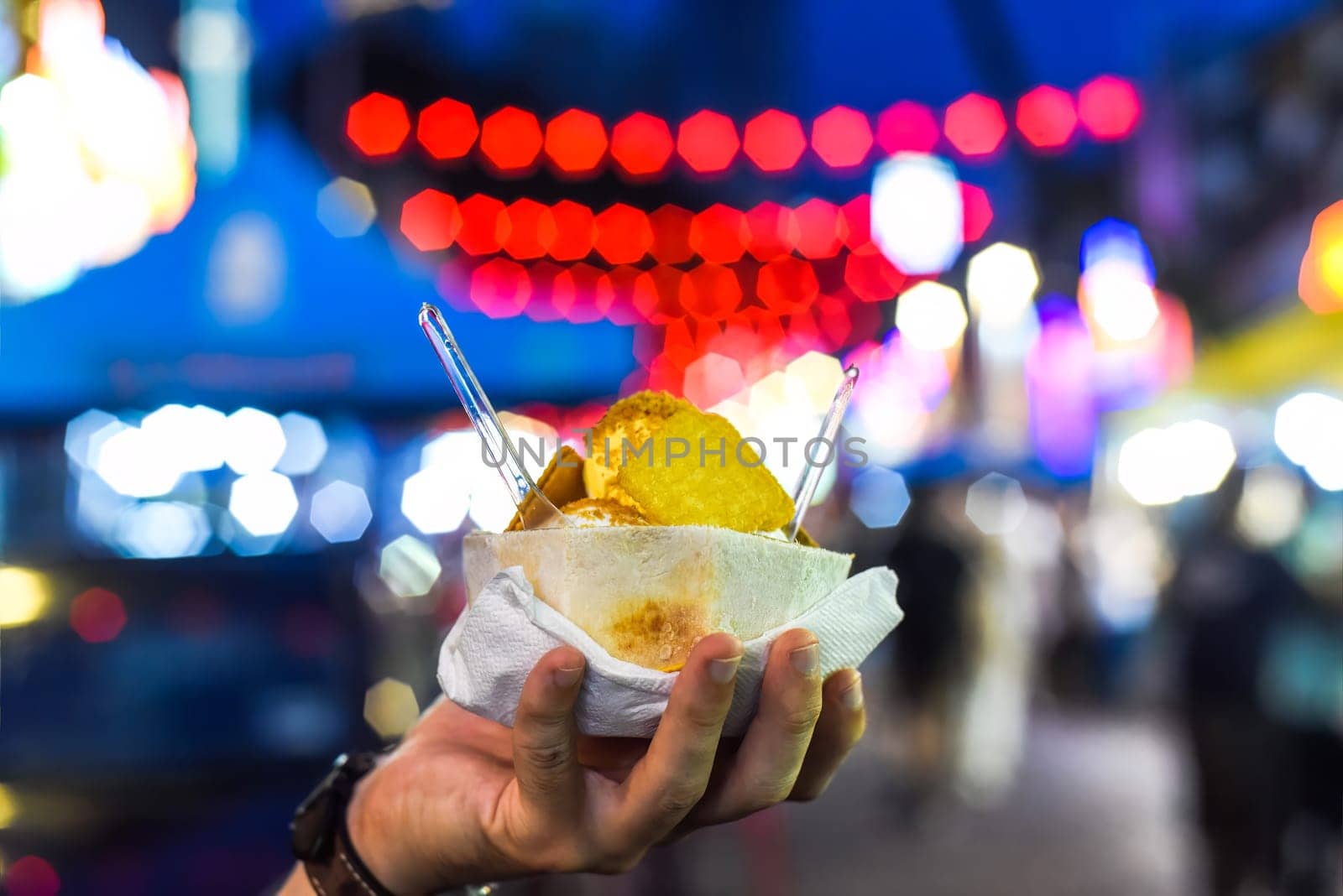 Hand holding coconut and mango ice cream in coconut shell against lights of Jalan Alor street food market in Kuala Lumpur