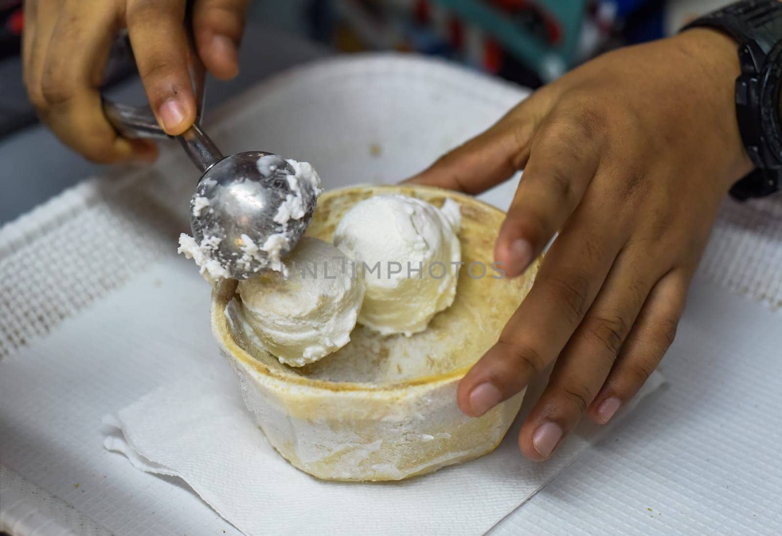 Hand holding coconut and mango ice cream in coconut shell in Jalan Alor street food market in Kuala Lumpur