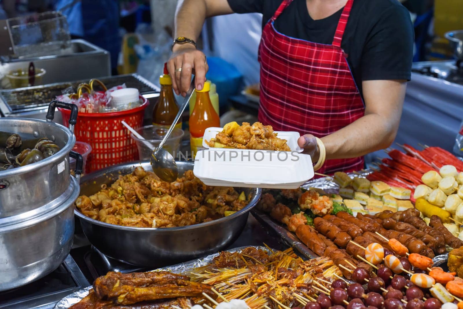 Vietnamese woman serving chicken paws in plastic box with chili in vietnamese night market