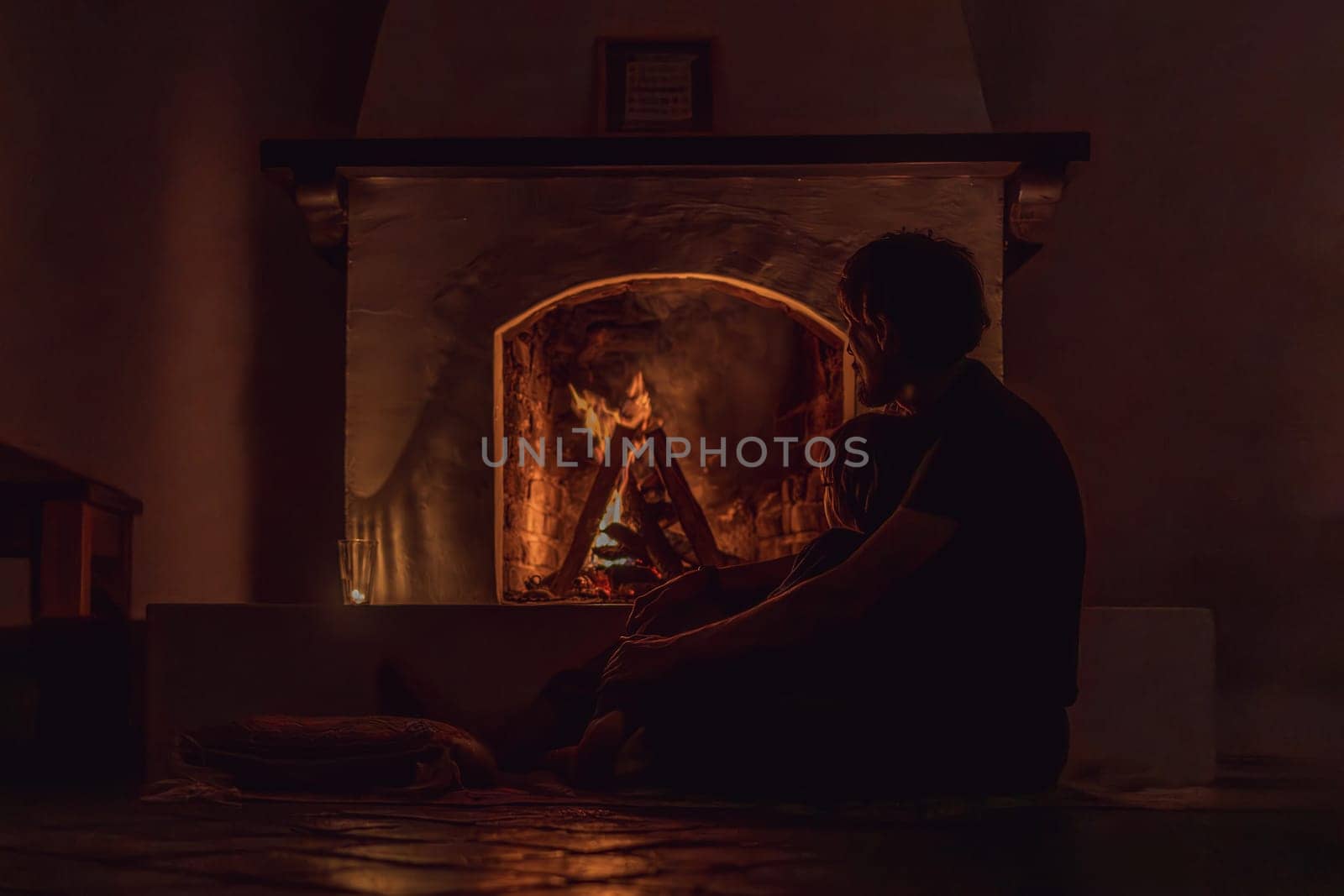 Family bonding by the fireplace during cozy winter evening. Warm and peaceful family moment indoors. Togetherness, love, and relaxation concept. A warm and inviting scene featuring a lit fireplace with glowing firewood and candles. A colorful traditional rug and pillow lie on the floor, creating a cozy atmosphere. Home, relaxation, and rustic comfort concept.