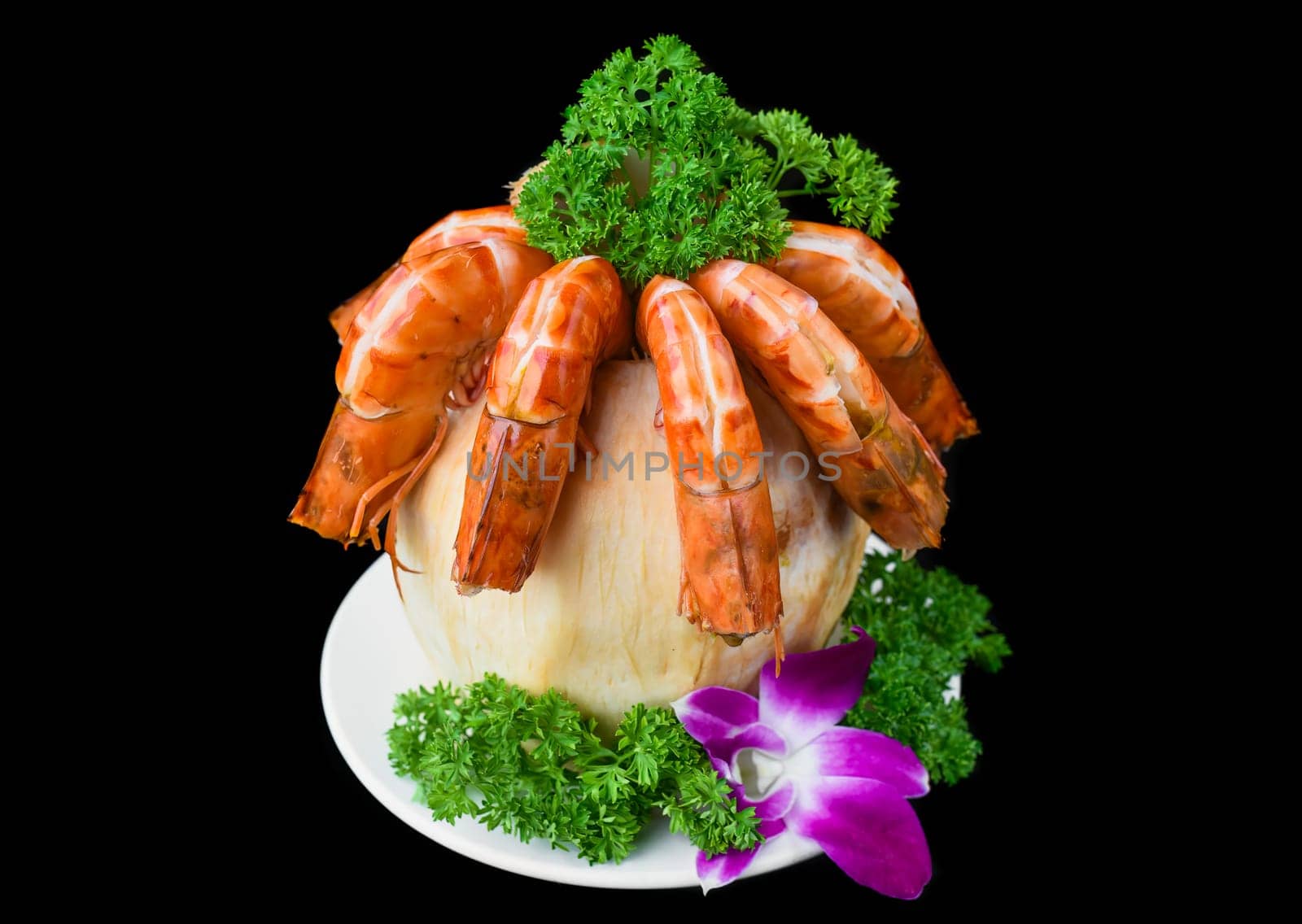 Orange shrimps inside of coconut with sauce isolated on black background side view