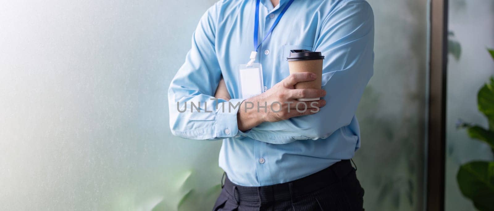 A business professional with crossed arms, holding a coffee cup, embodying a mix of confidence and casual professionalism in a contemporary workspace.
