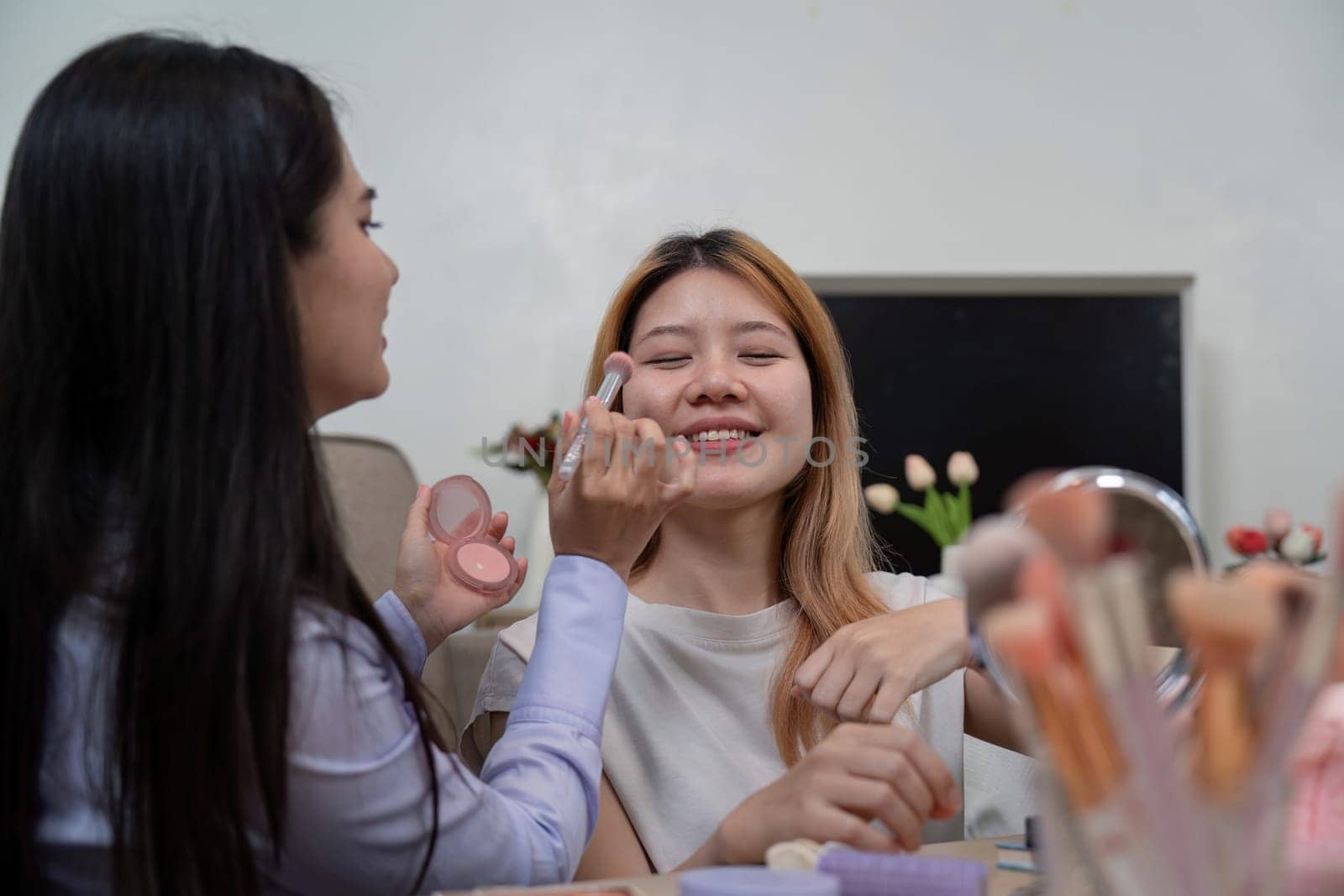 A beauty broker applying blush on a friend cheeks during a live broadcast, sharing beauty tips and enjoying a joyful moment together.