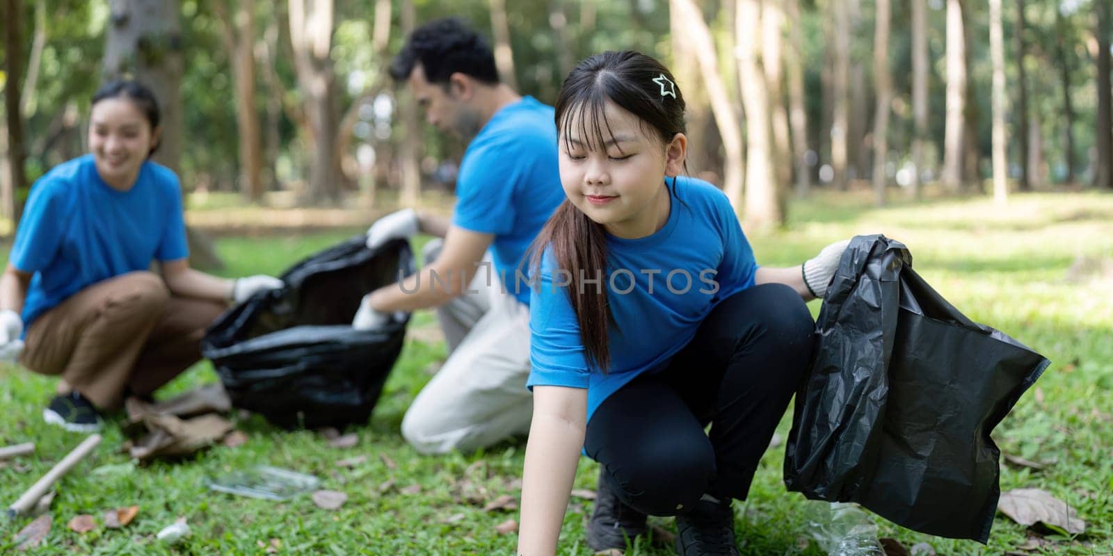 A family of volunteers diligently collects garbage in a park, showcasing their dedication to environmental stewardship and teamwork.