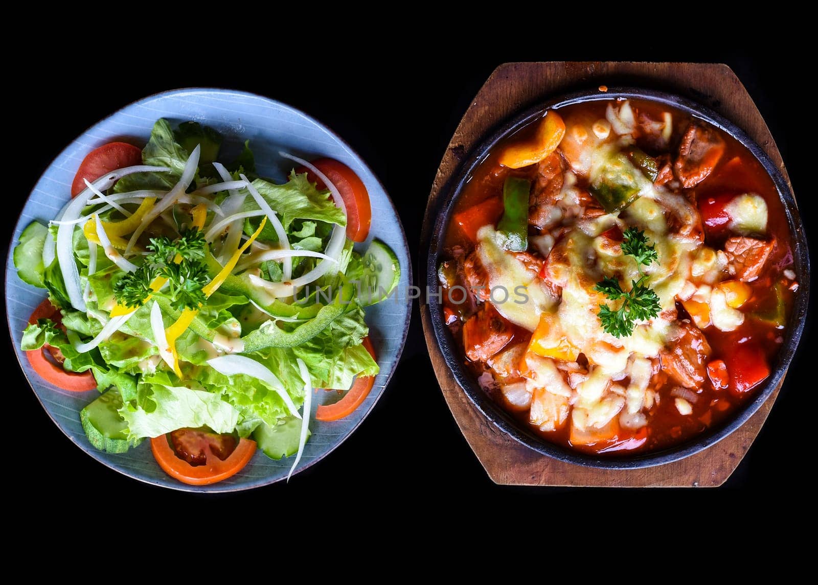 Stewed beef with cheese and vegetables on wooden plate isolated on black background side view