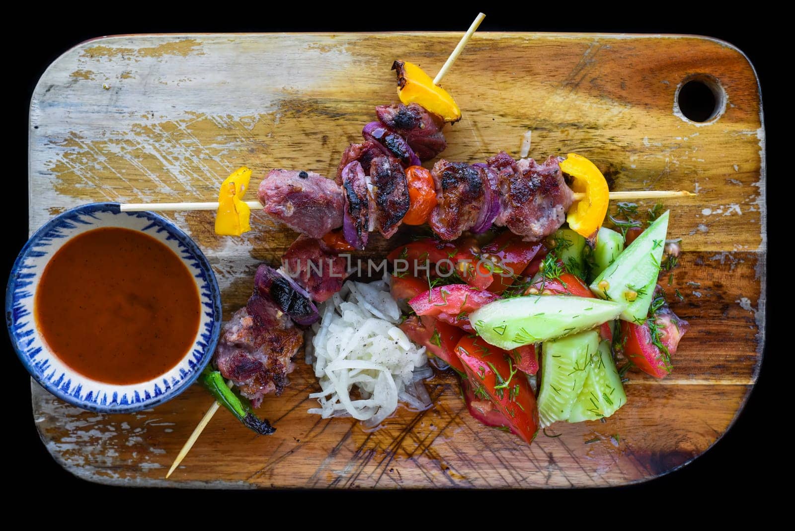 Pork skewers served with salad and sauce on black background top view