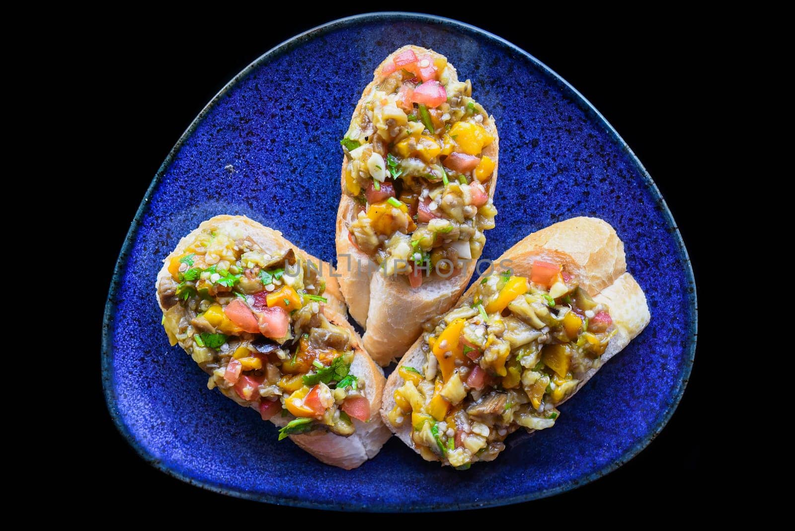 Vegetarian Bruschetta with tomatoes, eggplant, pepper and olive oil on blue plate close up