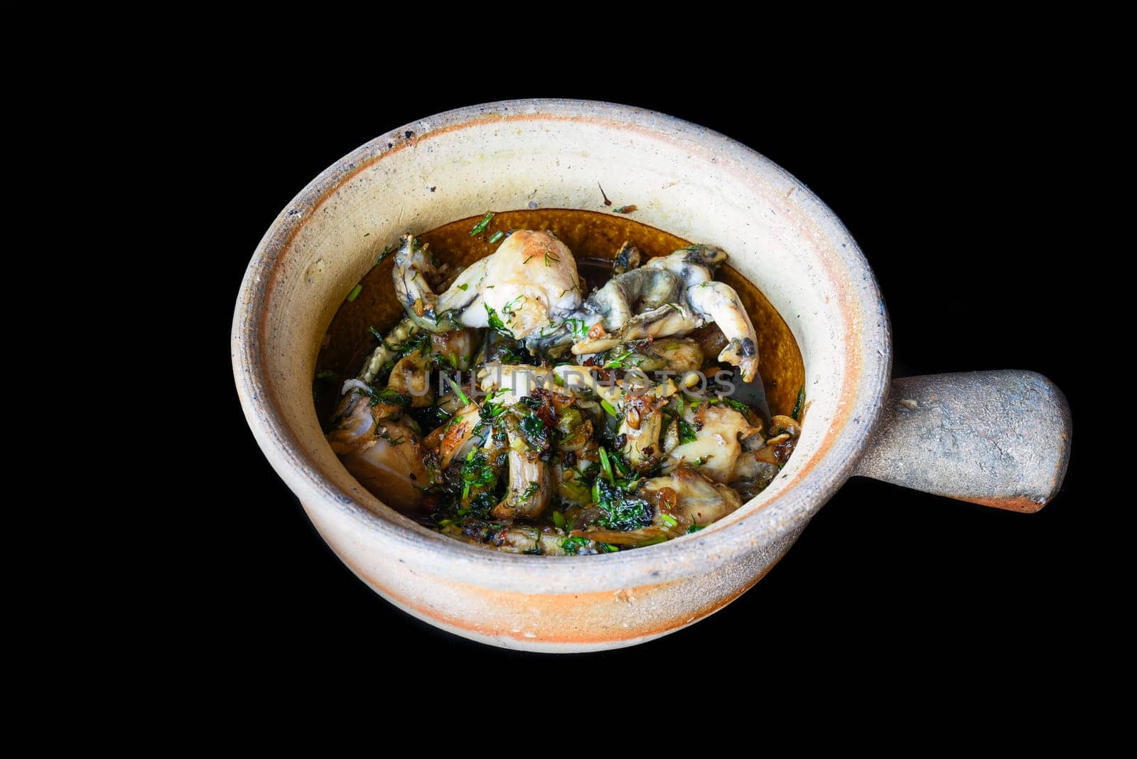 stewed frog stew in a pot isolated on black background close up
