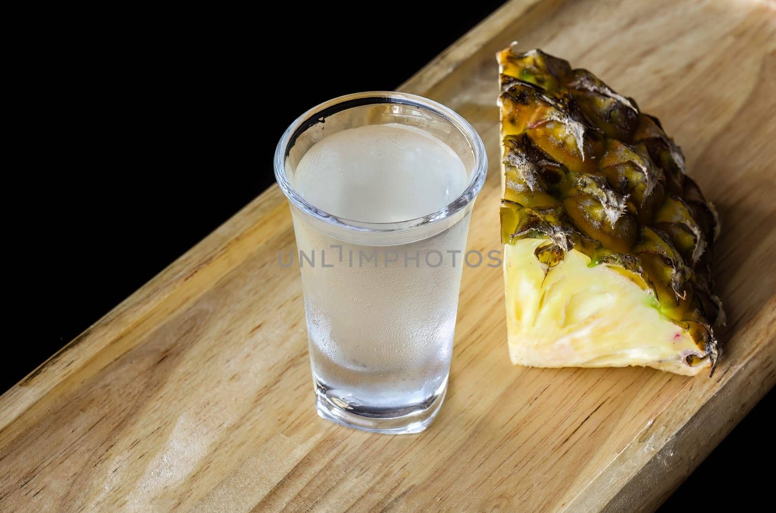 Alcohol shot made of pineapple juice on wooden board with copy space