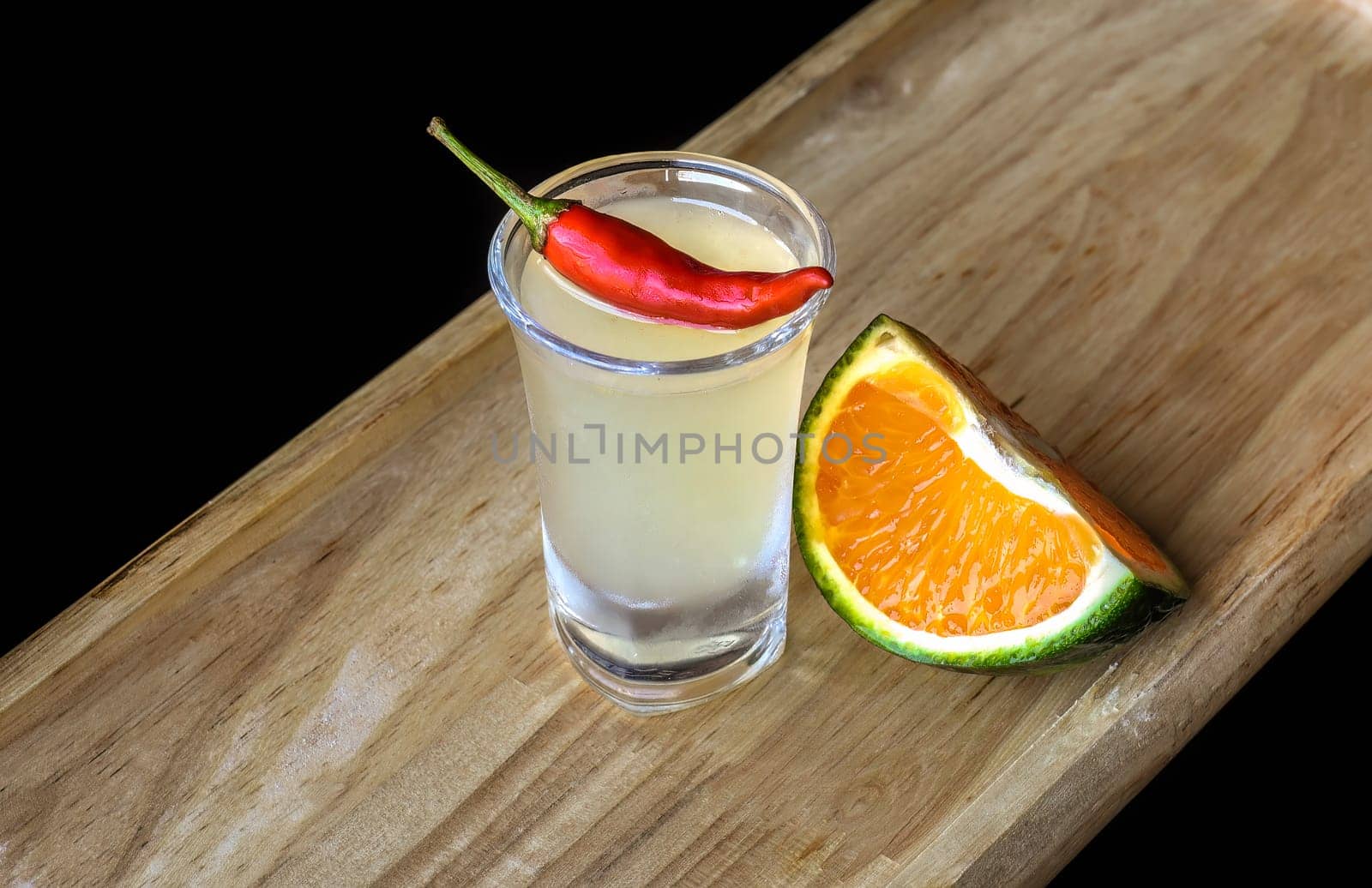 Alcohol shot made of orange juice and chili on wooden board with with copy space