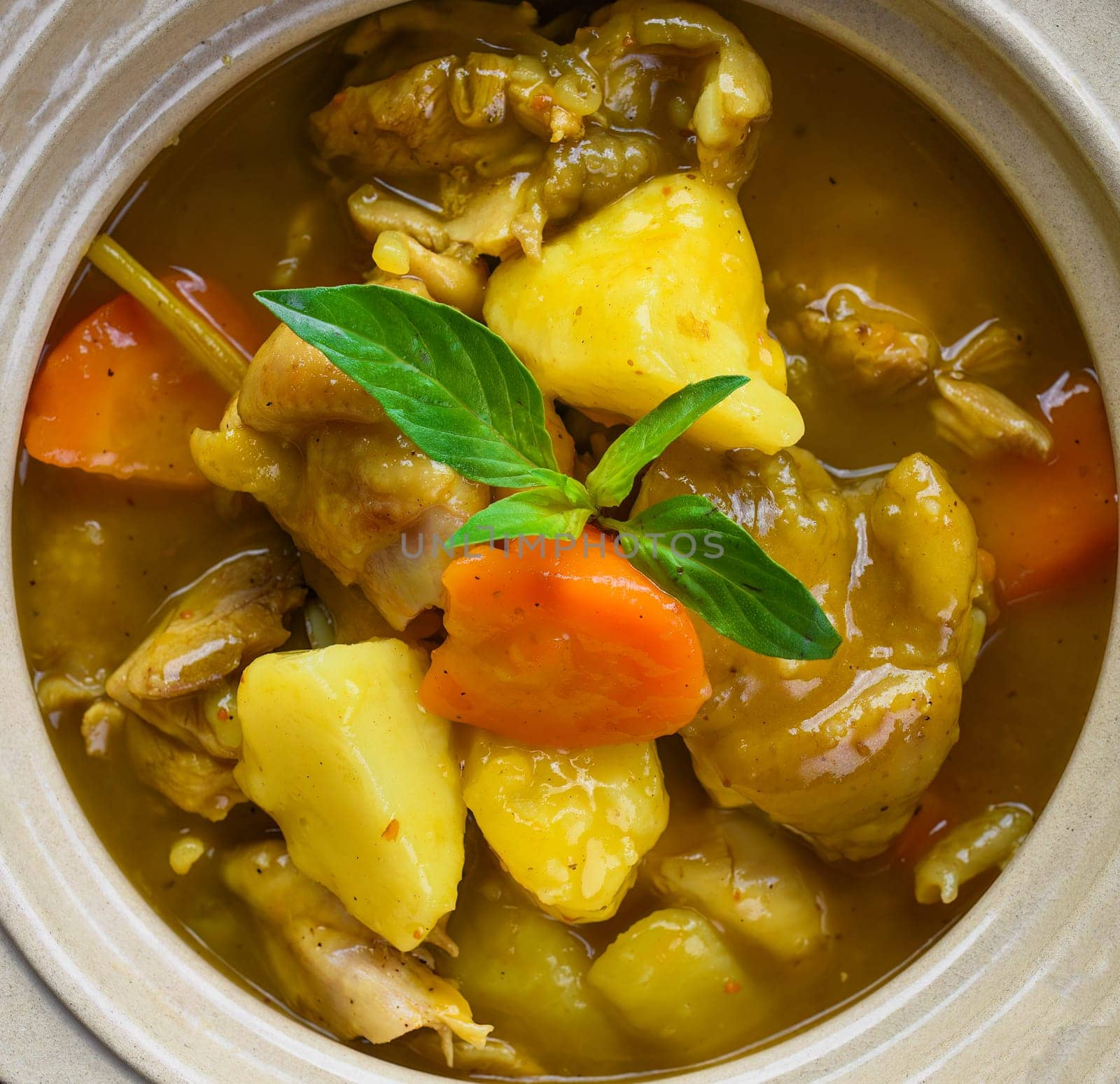 Stewed chicken with potato and vegetables on blue plate isolated on black background top view