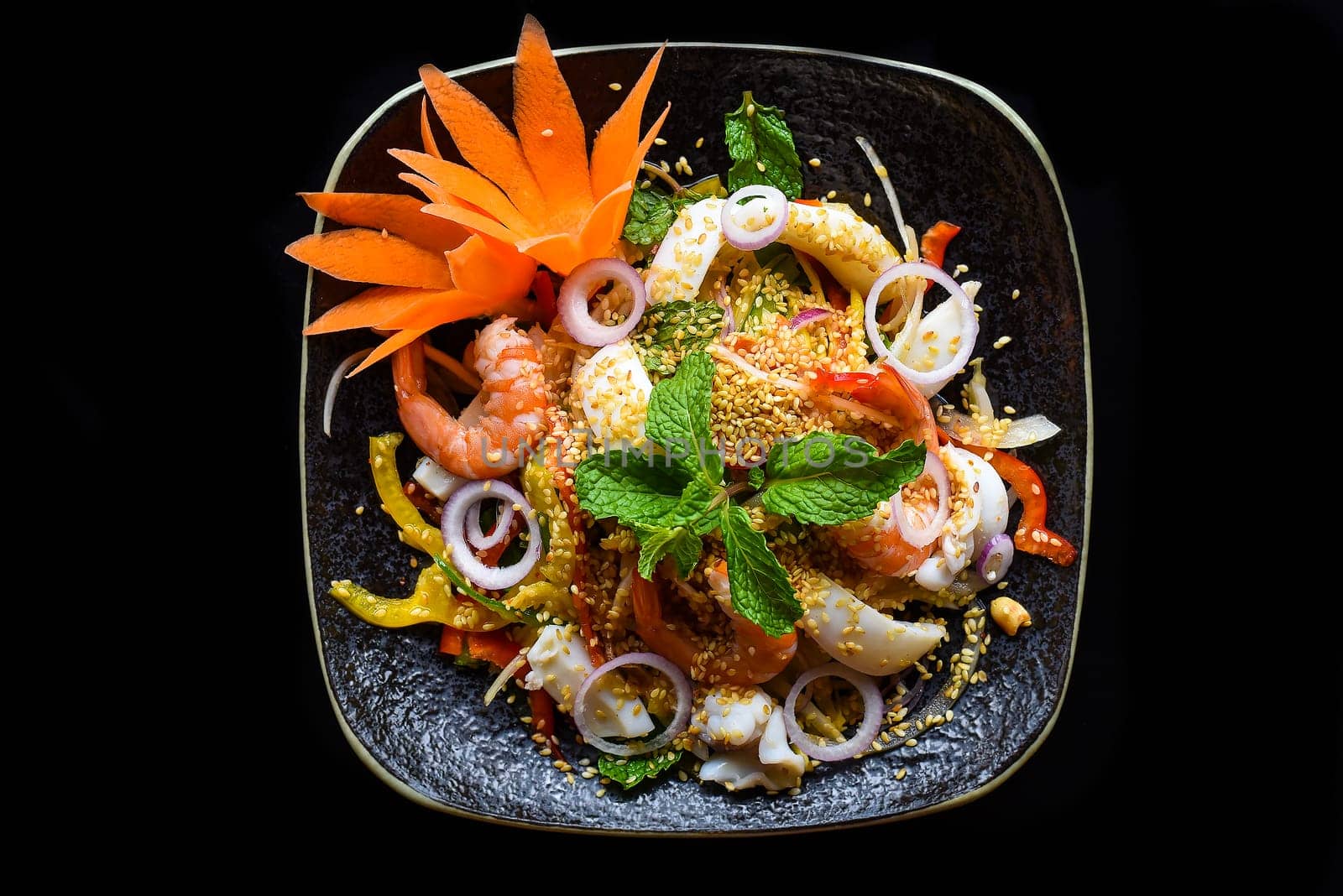 Thai salad made of shrimps and squid and onions isolated on black background side view