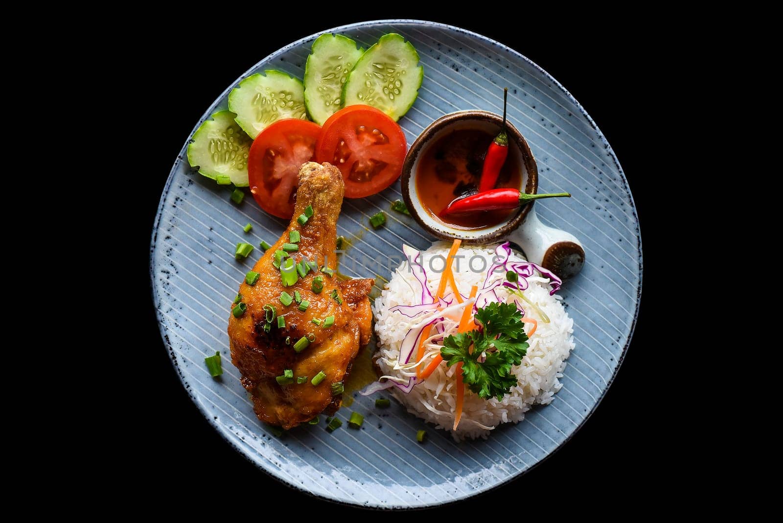 Roasted chicken leg in Vietnamese style with rice, vegetables and sauce isolated on black background top view