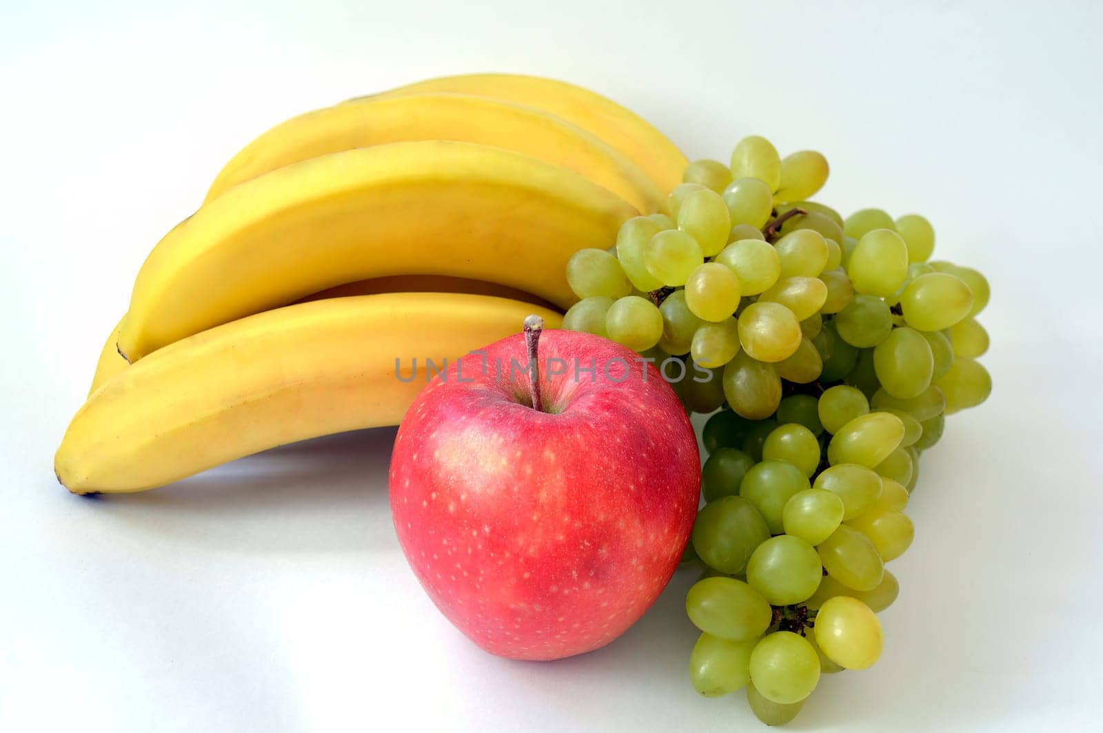 Big red apple in front of the bunch of bananas and ripe indian green grape isolated on white background