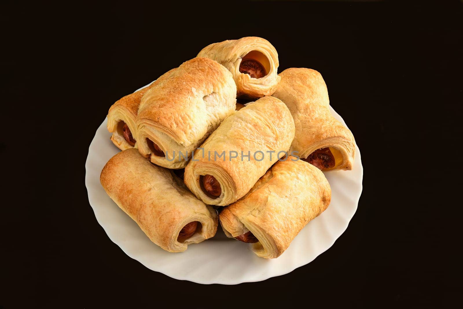 Many sausage rolls (pigs in a blanket) on white plate on black table