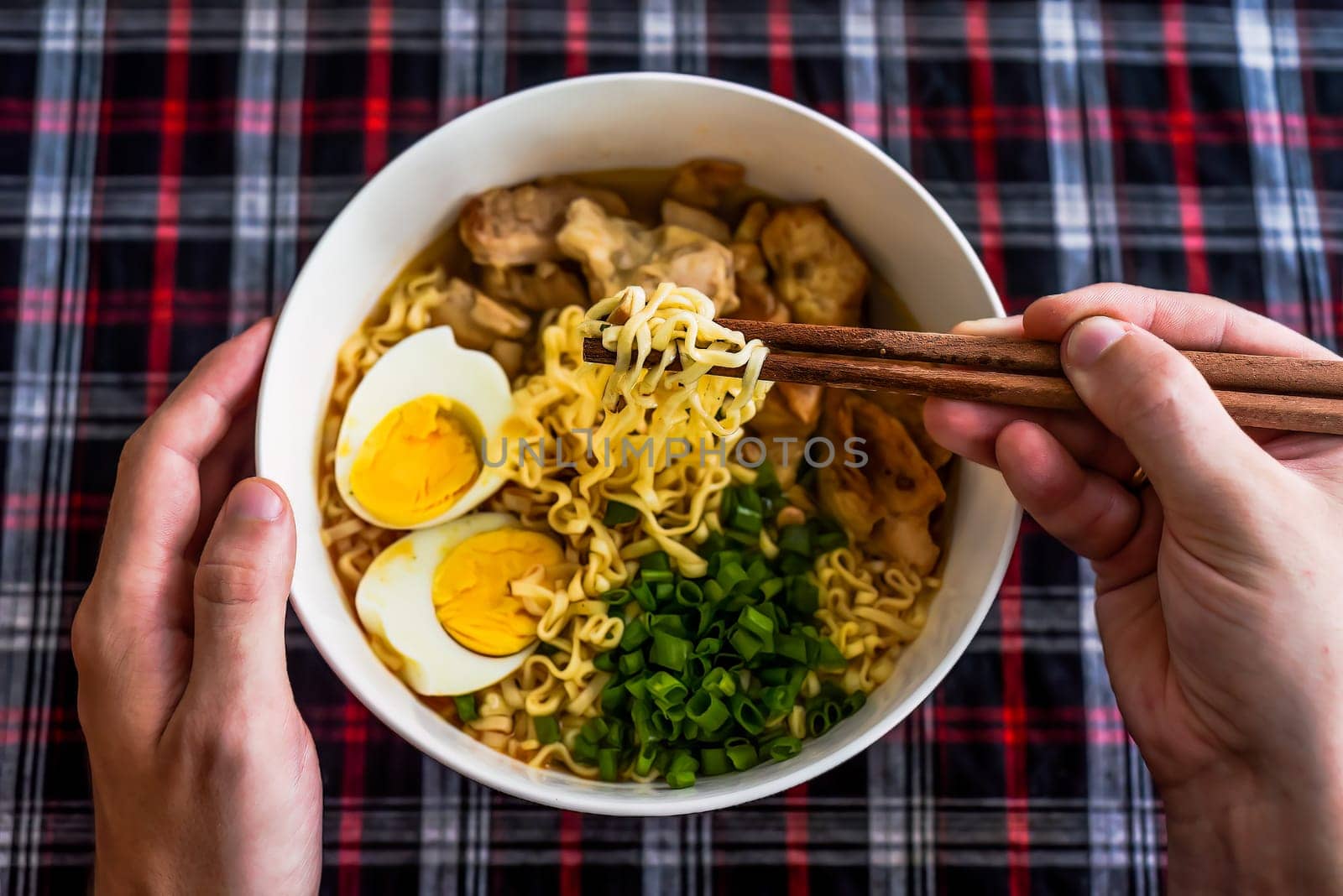 Piece of chicken in chopsticks with japanese ramen and males hands