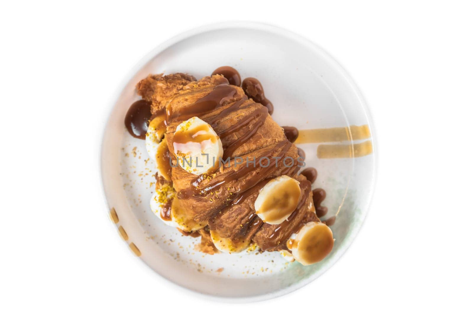 Sweet croissant with banana, salt caramel and fresh cream in white plate on white background