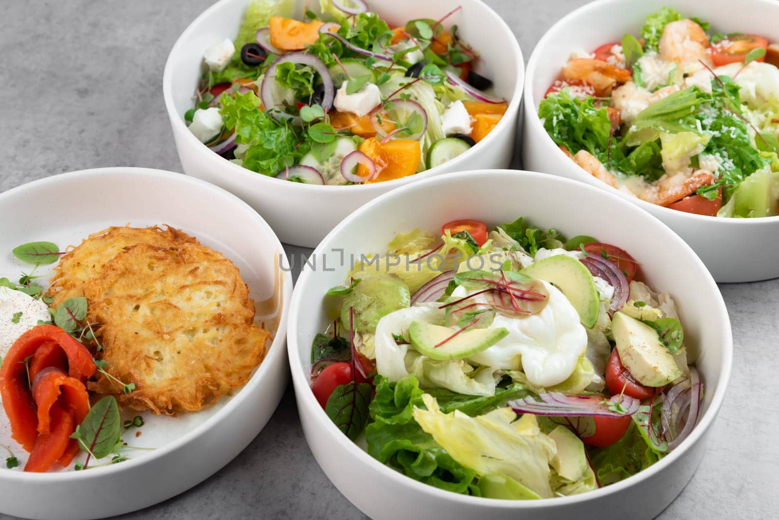 Three different vegetable salads and slavic draniki (potato pancakes) on gray marble background