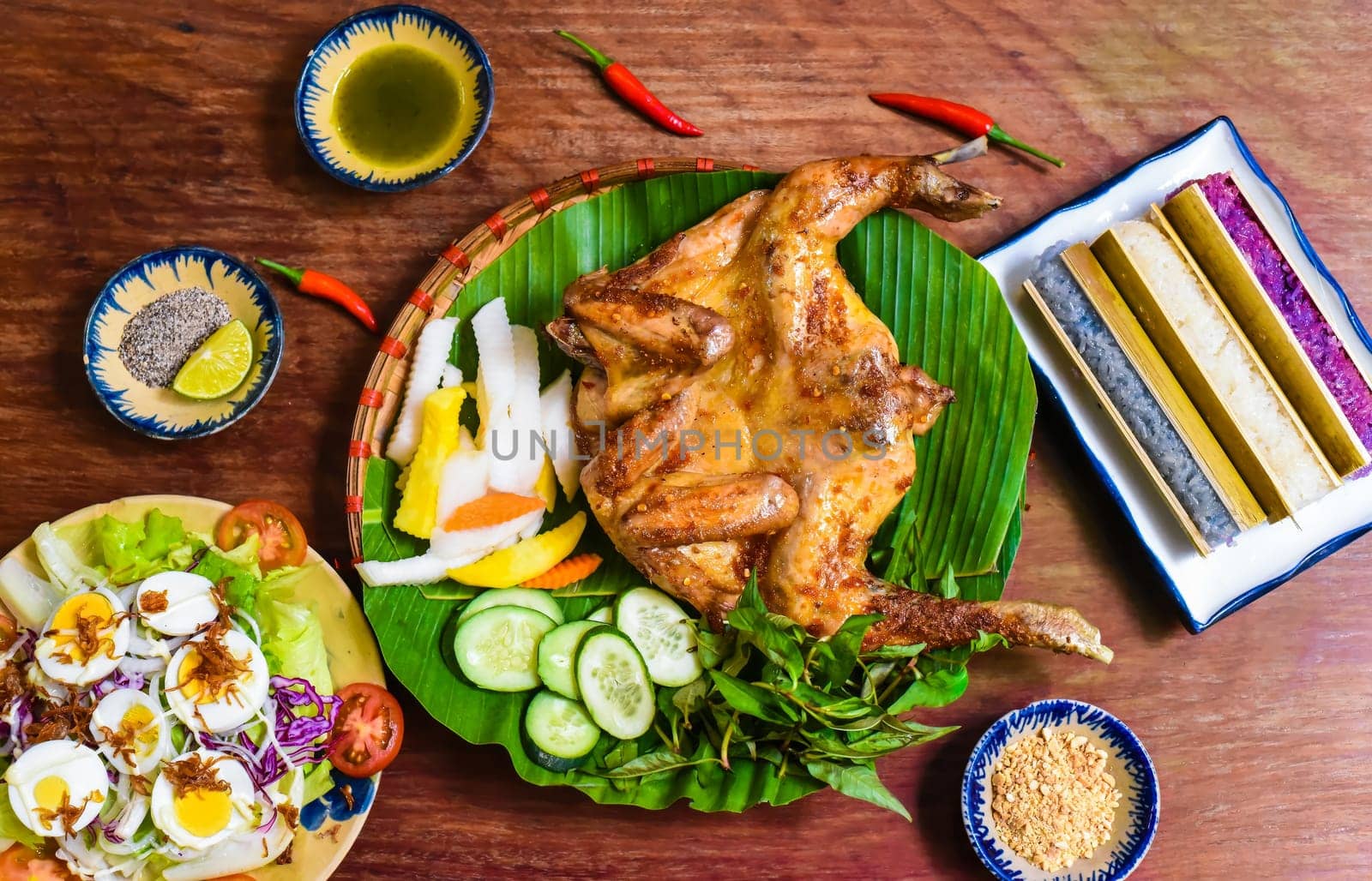 Grilled chicken in vietnamese style with colorful rice in bamboo, and boiled eggs on wooden table