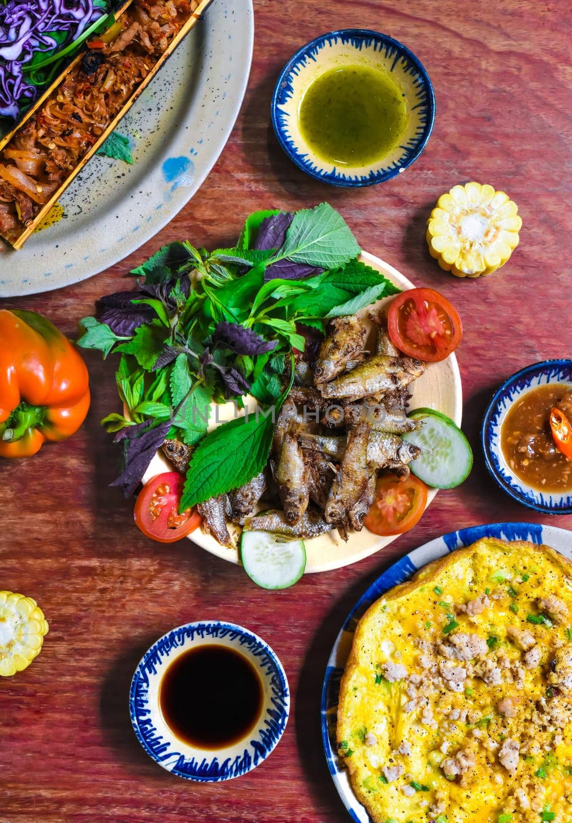 Vietnamese cuisine set made of braised deer in bamboo, fried fish, omelette with sauces on wooden table