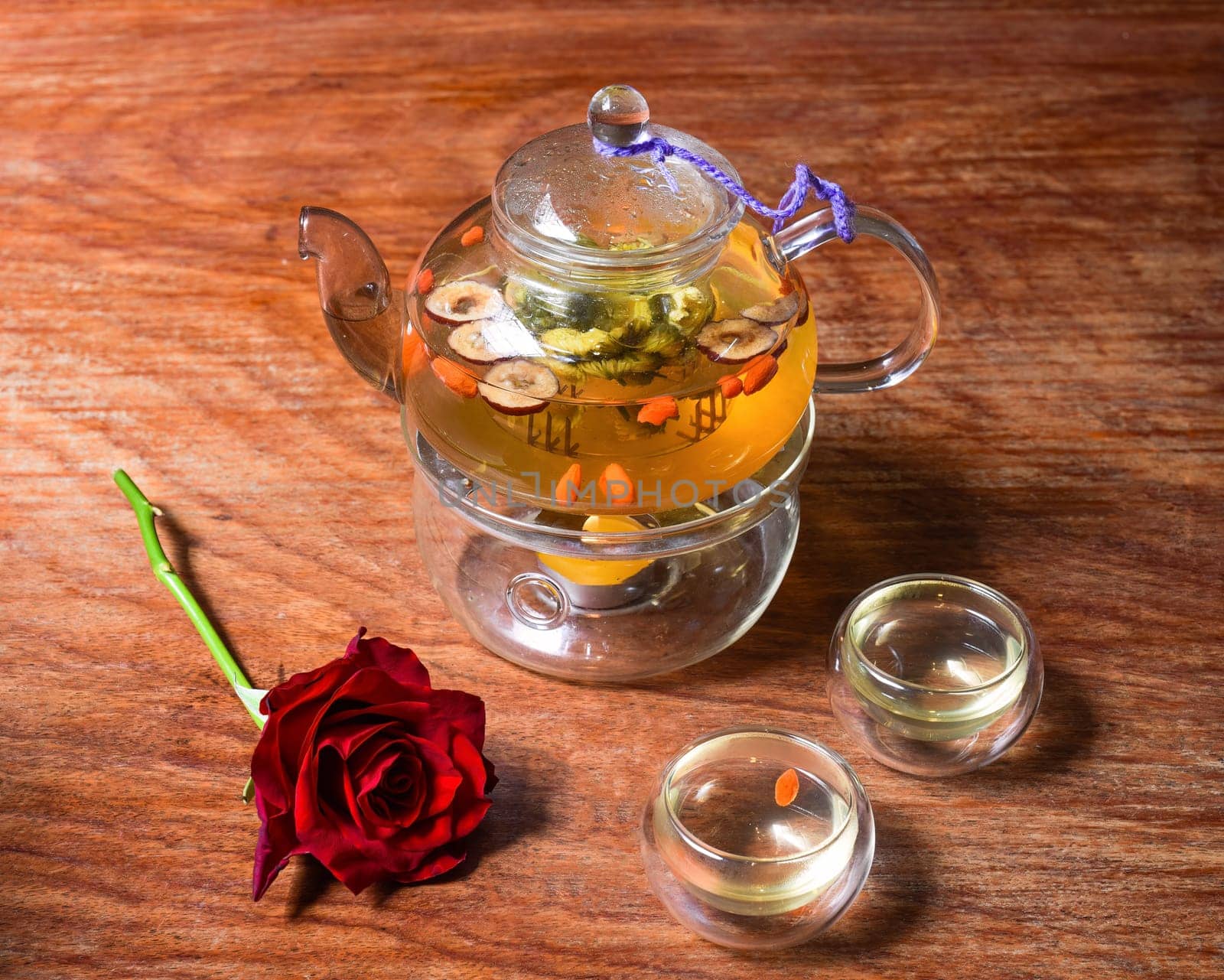 Chamomile tea with goji berries and flowers with cups and rose flower on wooden table