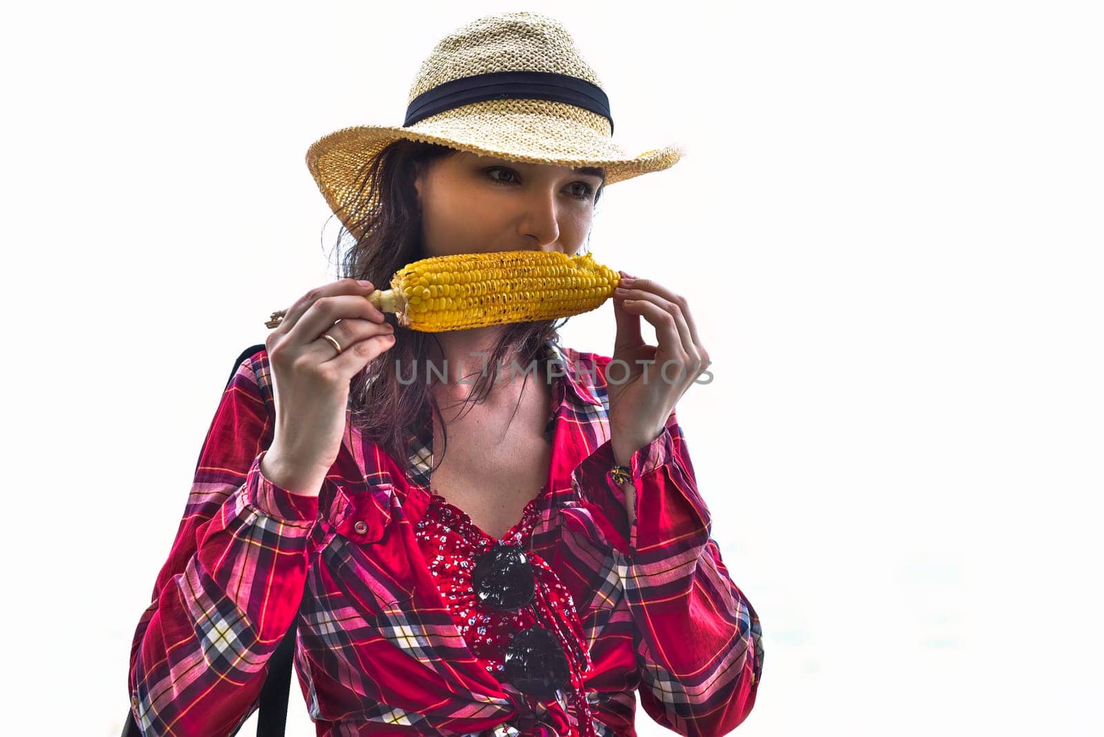 Young woman in hat eating grilled corn against white background