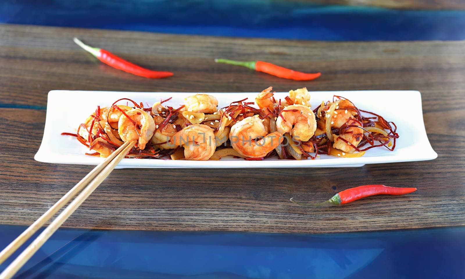Grilled shrimp with onions and chili on a white plate on the table. For asian food menu