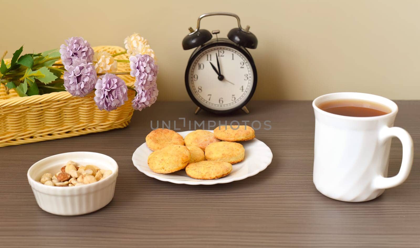 Round homemade curd cookies on a plate next to cup of tea and basket with flowers