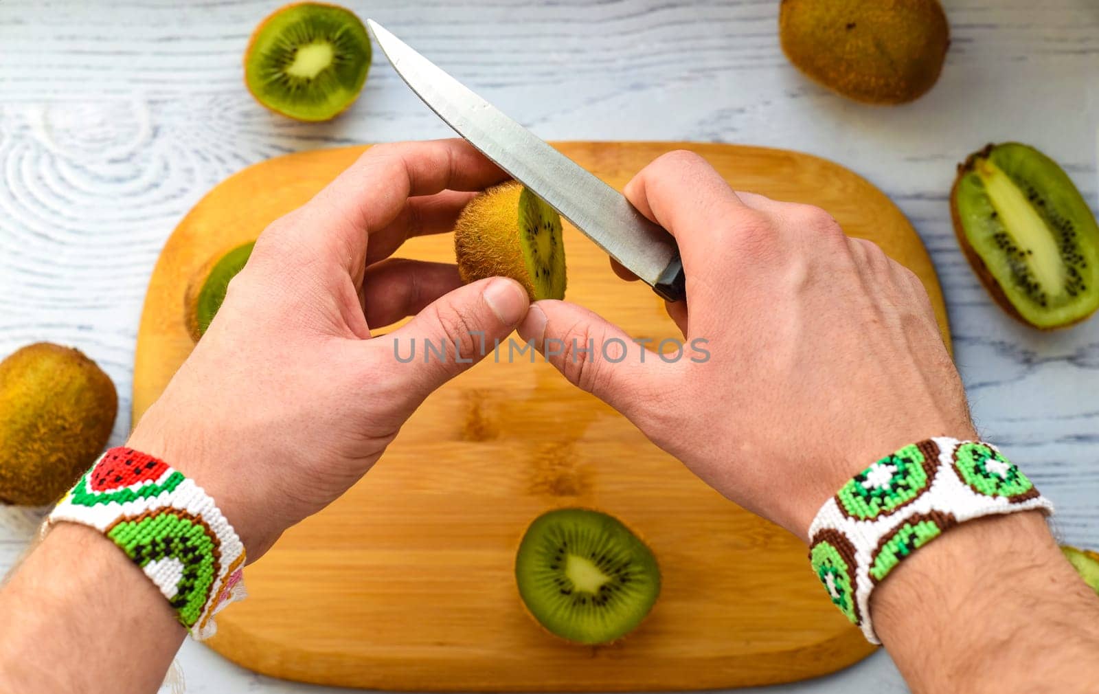Hands cutting kiwi over cutting board.