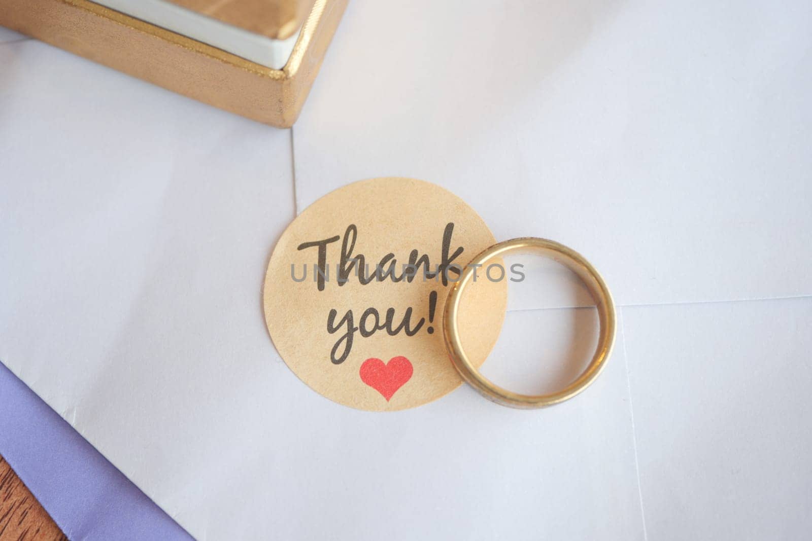 A gold ring resting on a thank you note on a table.