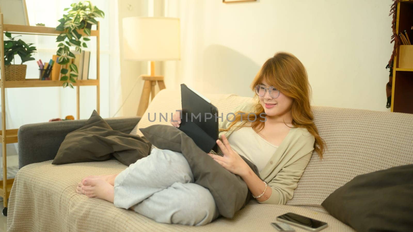 Relaxed young woman using digital tablet in bright living room.