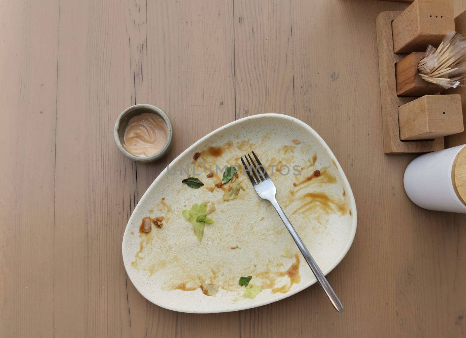 Dirty plate after dinner. Top view of dirty white plate with fork over wooden tabletop. Dirty plate after eating salad with sauce on the dining table. Copy space