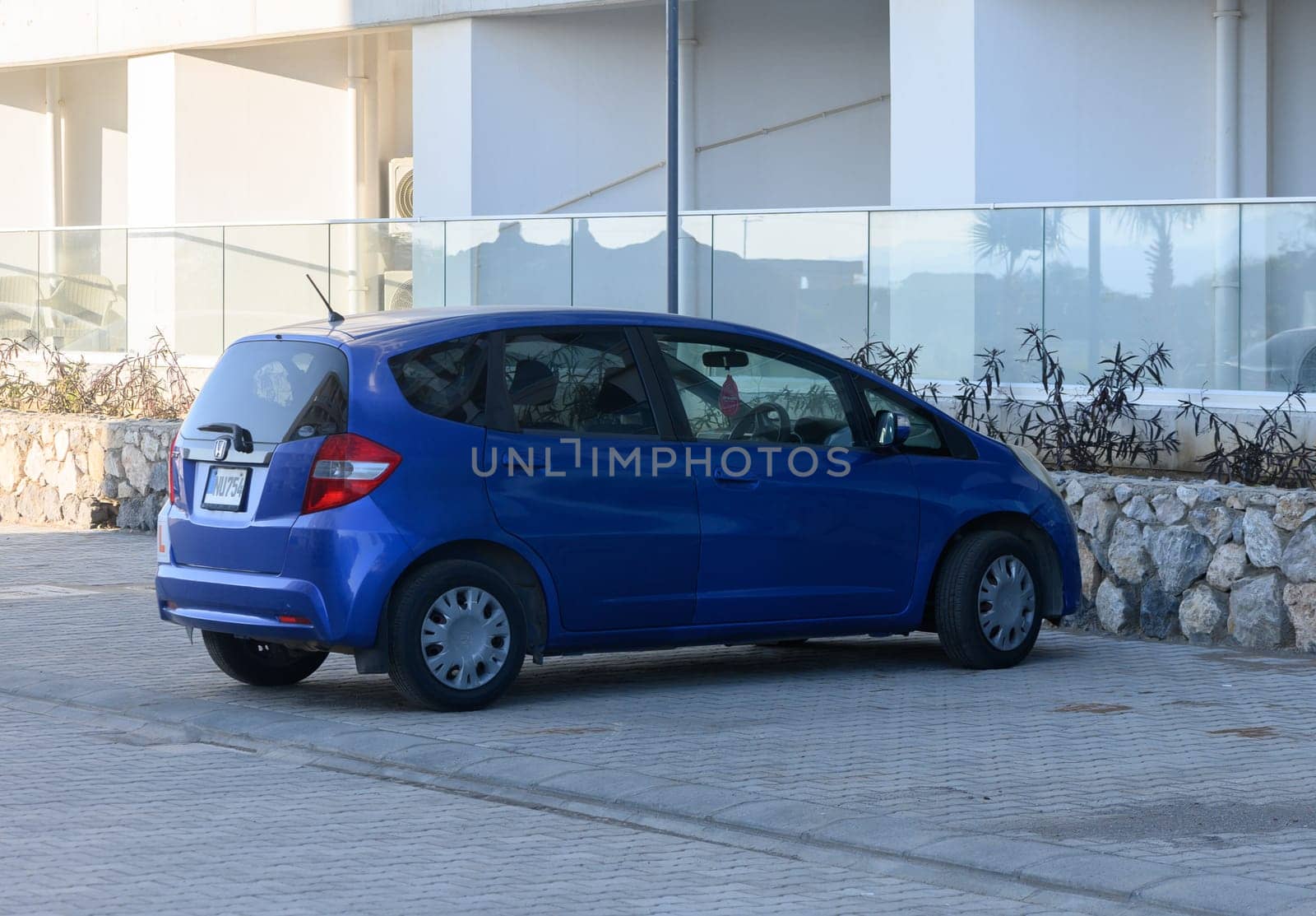Gaziveren Cyprus -03.02.2025 A compact blue car rests beside the shore, with gentle waves crashing nearby and a clear sky overhead.