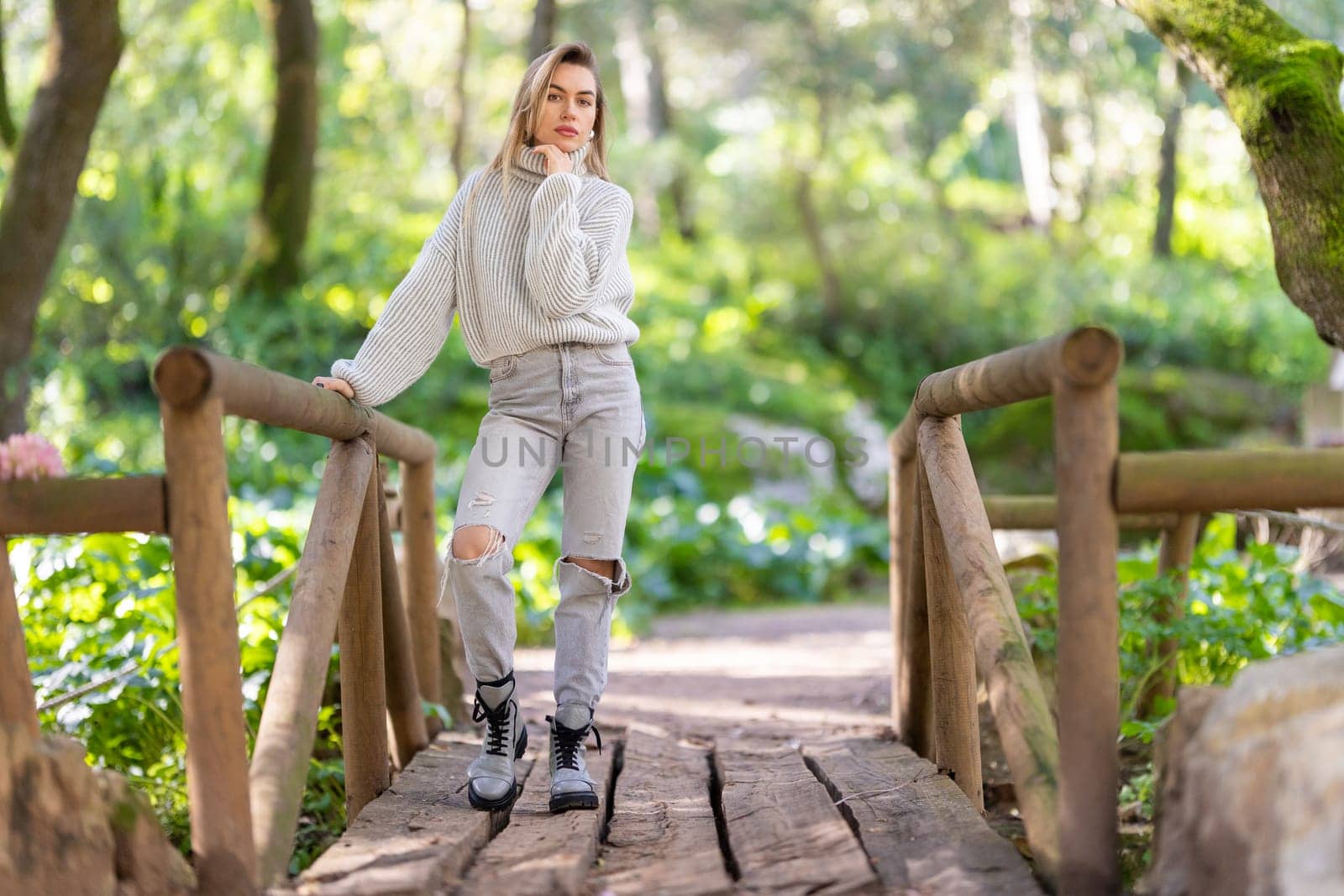 Young woman wearing casual clothing is standing on a wooden bridge in a forest