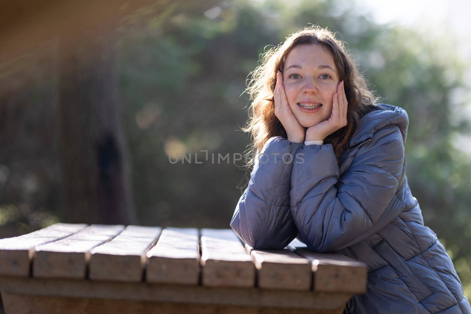 Happy teenager with dental braces smiling and posing with hands on face in a park