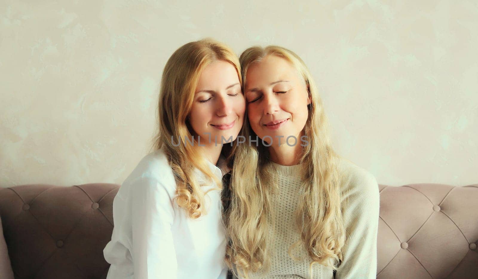 Portrait of happy smiling caucasian middle aged mother hugging her adult daughter together sitting on couch at home