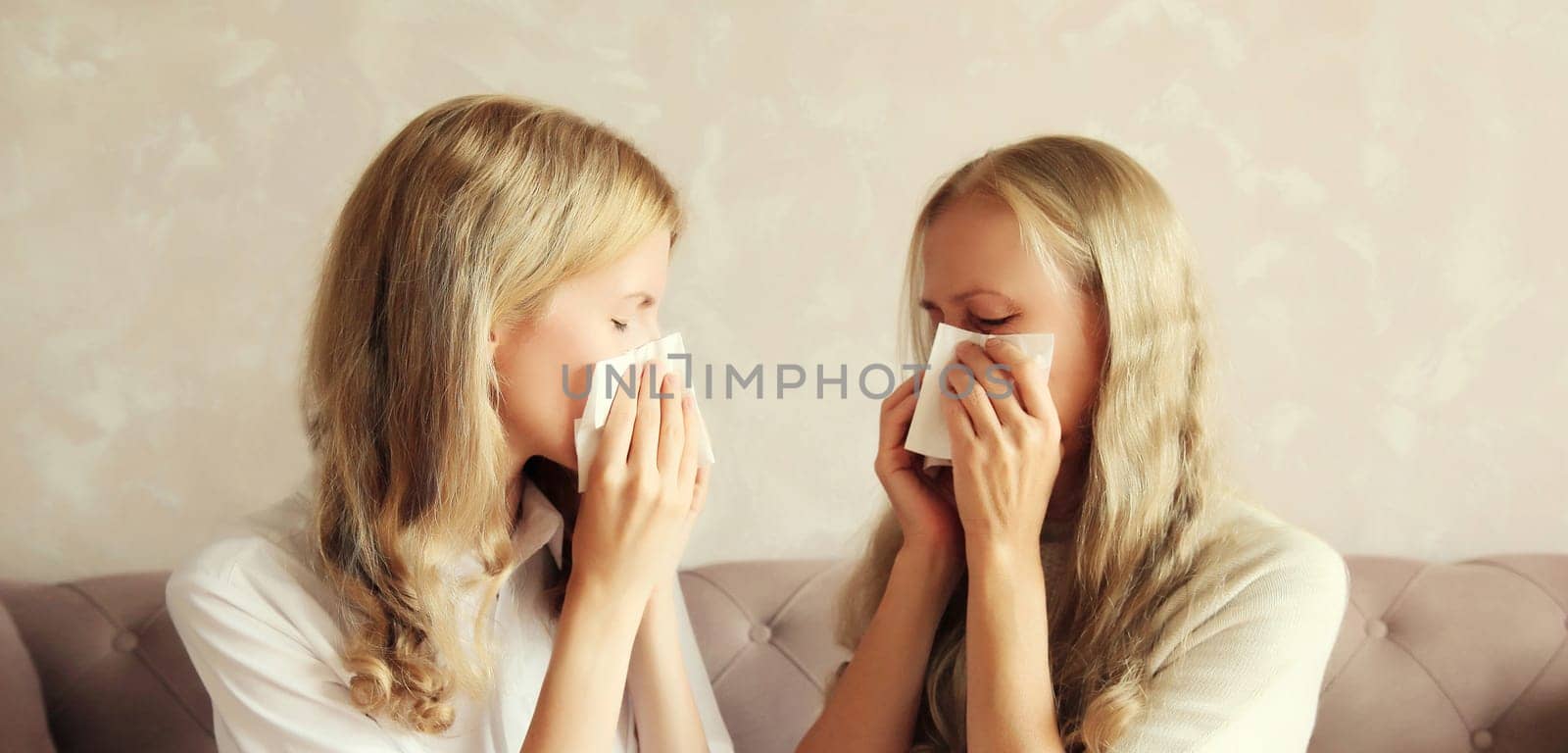 Sick exhausted middle-aged woman mother and adult daughter together sneezing blow nose using tissue at home