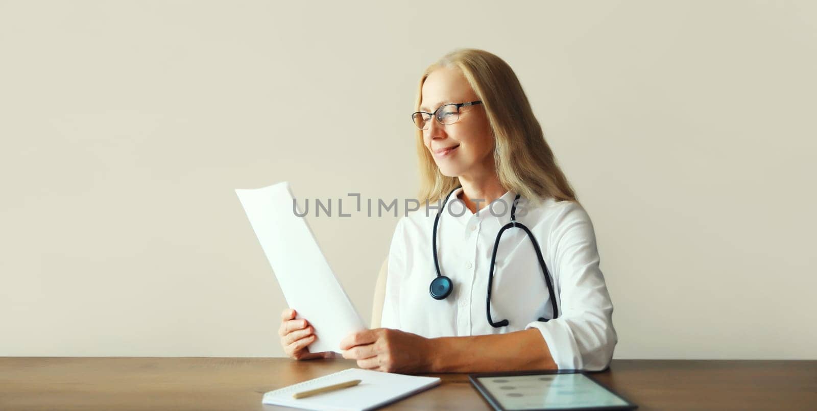 Caucasian middle-aged woman doctor working sitting at desk in clinic office