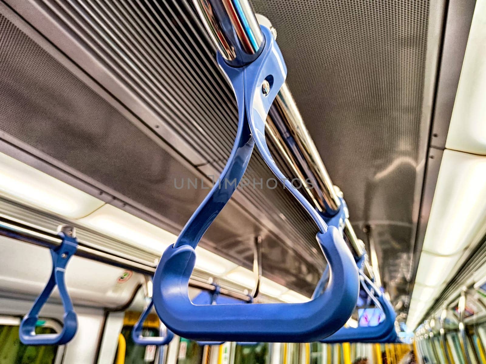 Close-up view of a blue handrail in a subway train with commuters in the background, highlighting public transport usage during rush hour.