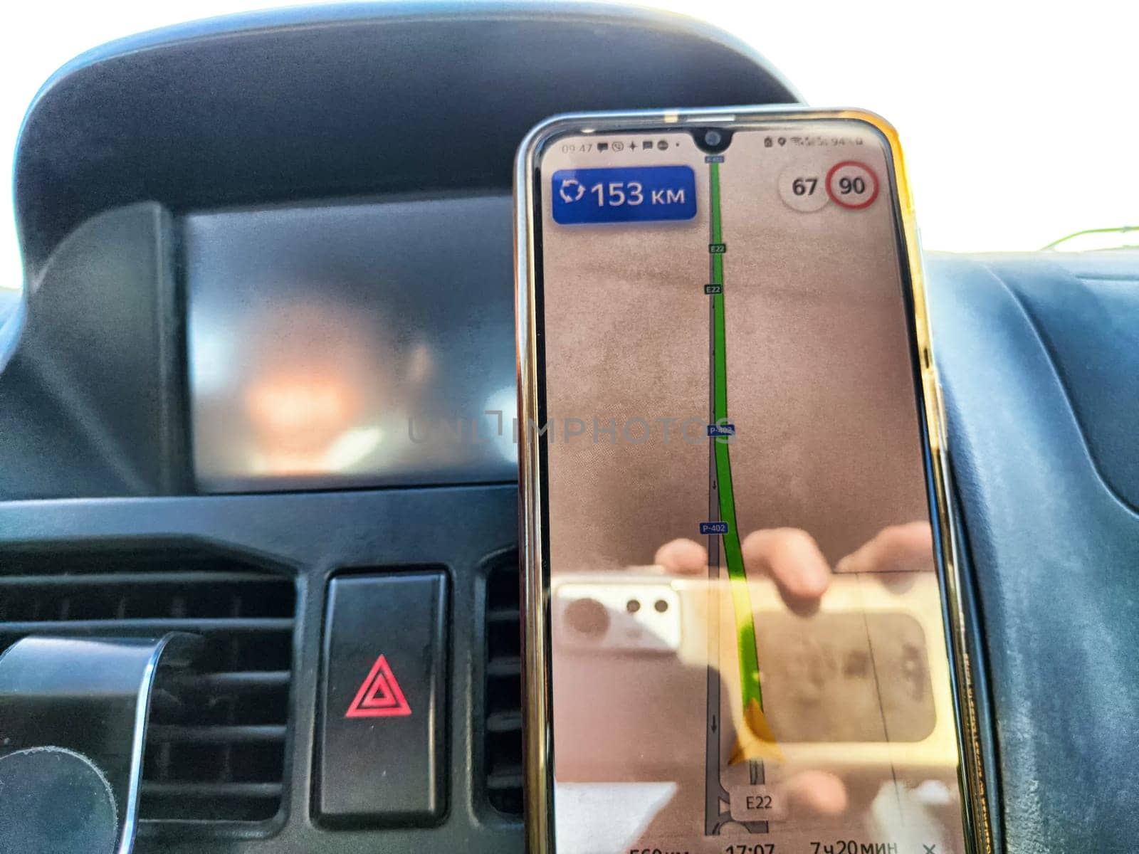 A smartphone shows a navigation map with distance and speed information while being held within the car during a trip.