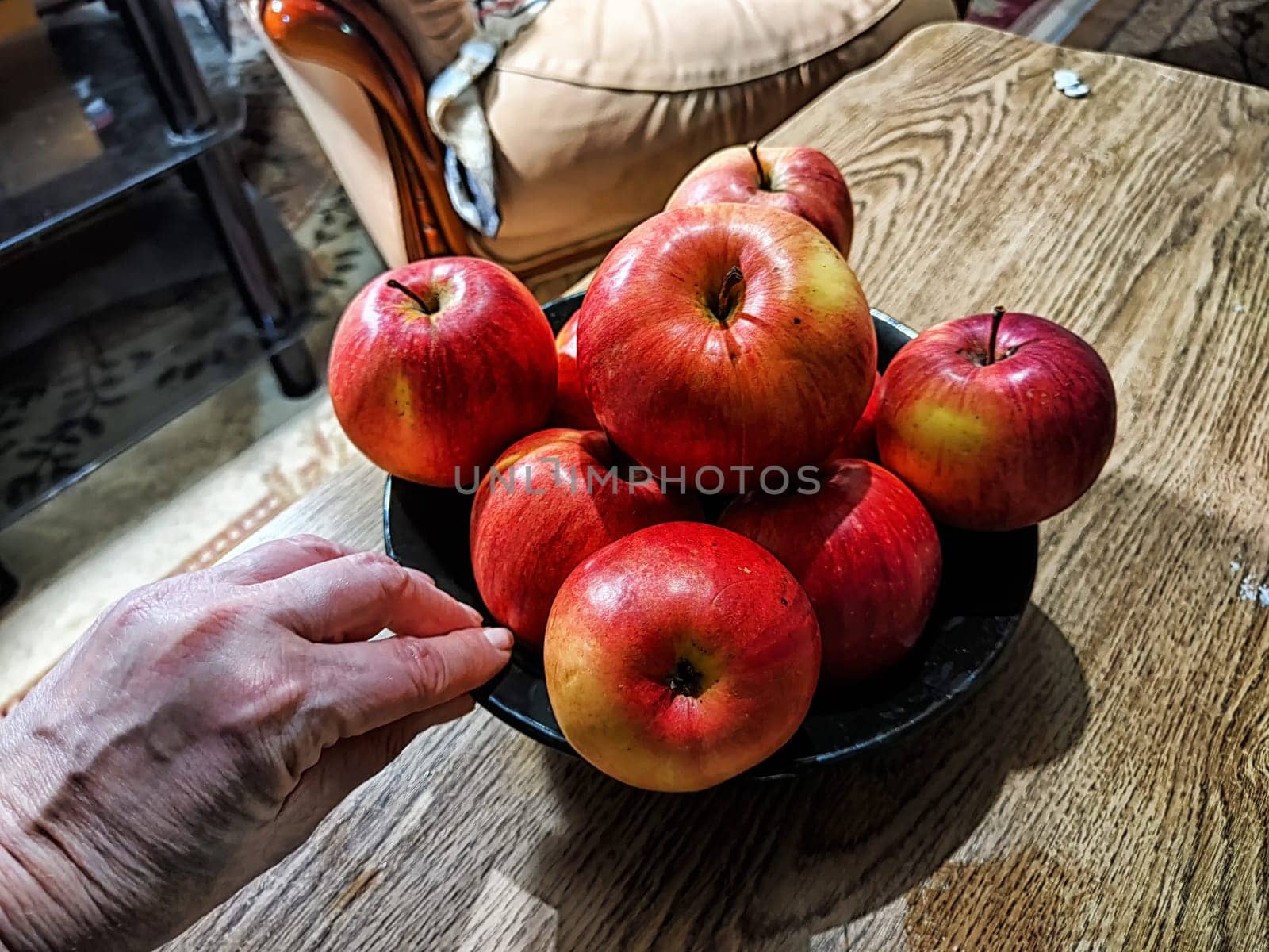 A hand reaches for a bright red apple in a bowl filled with shiny, fresh apples on a rustic wooden table.