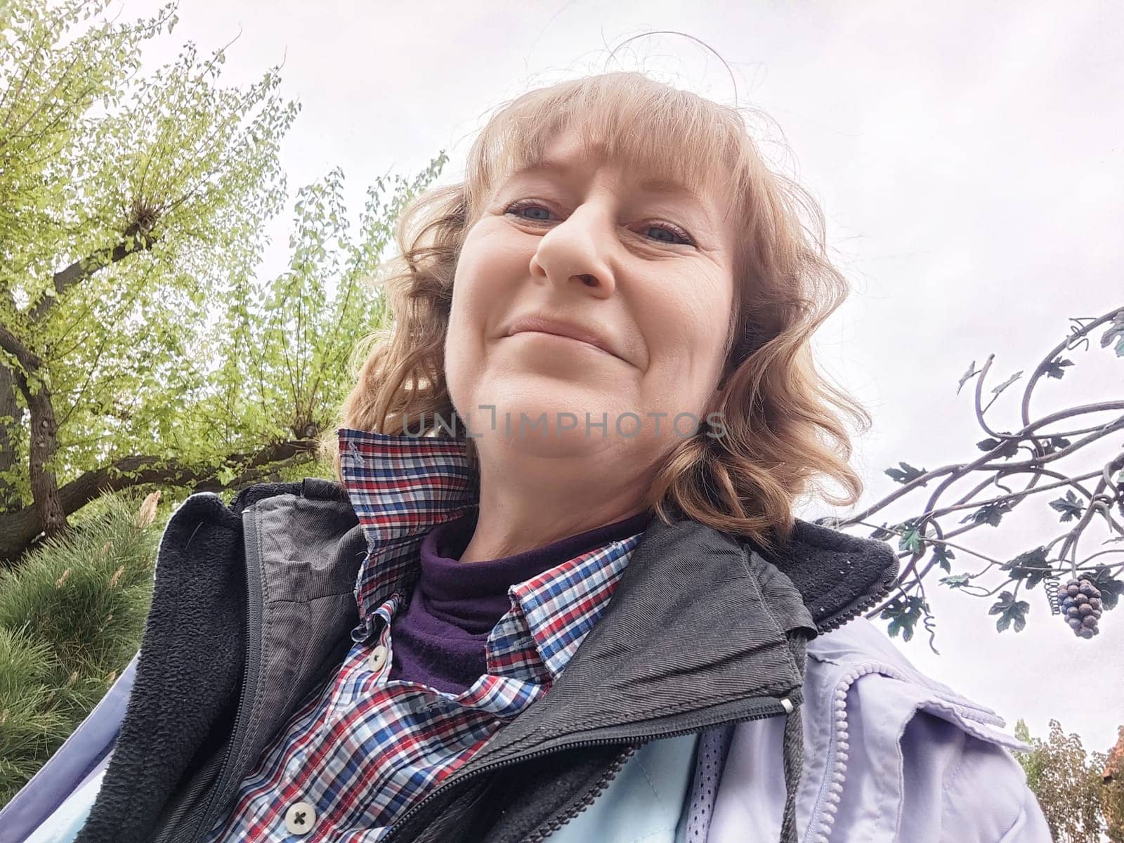 Blonde woman captures a cheerful selfie while exploring nature in a park on her travel journey.