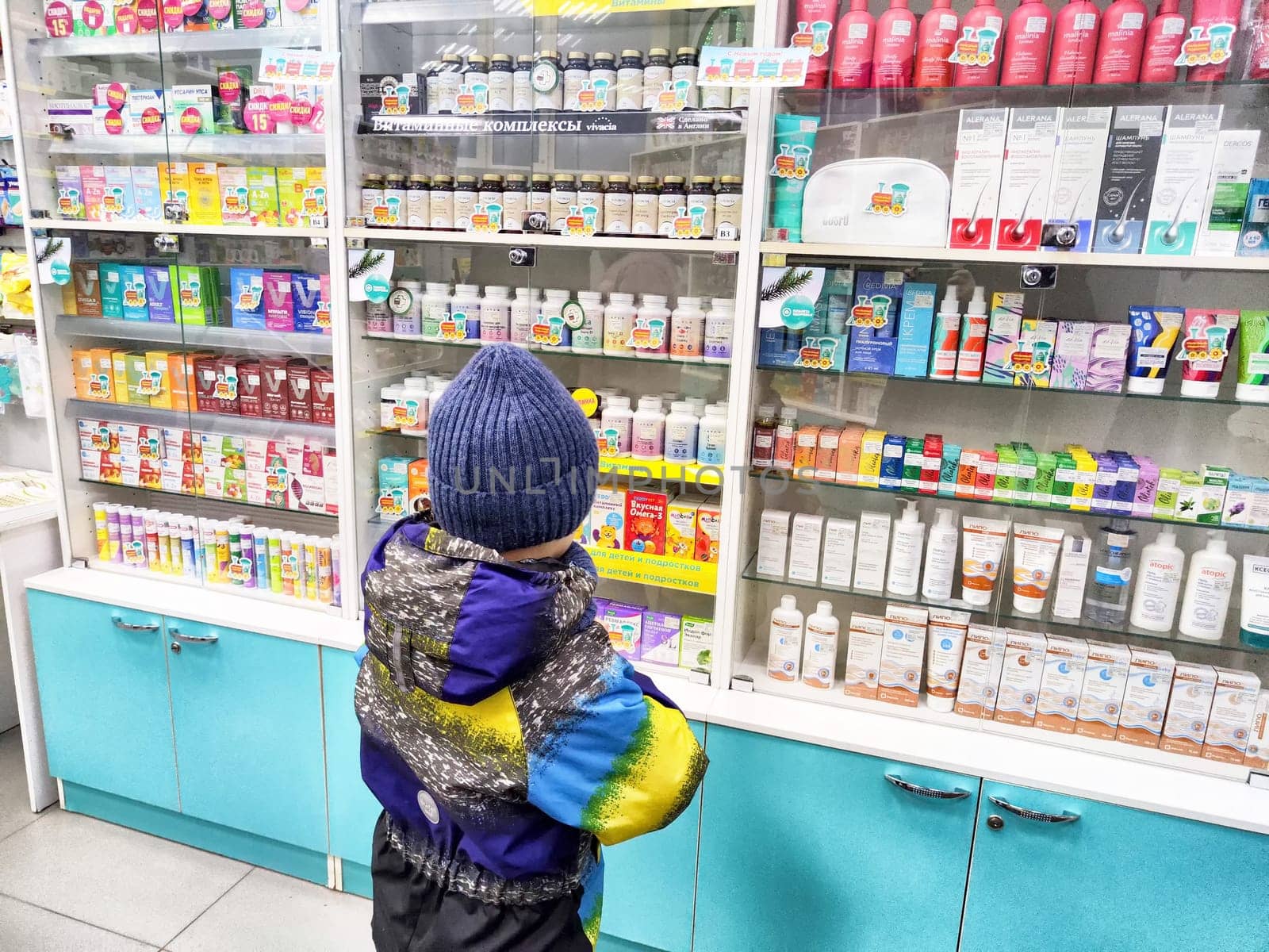 Kirov, Russia - December 28, 2024: Young child stands at a pharmacy counter, observing various health products and medicines on display.