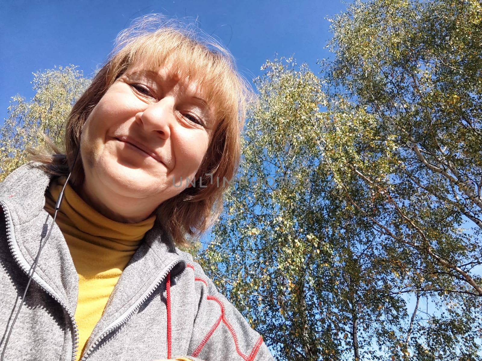 Blonde woman captures a joyful moment on her nature adventure, surrounded by vibrant autumn foliage and clear blue skies.