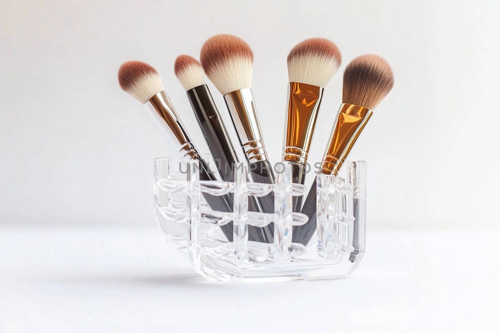 Five stylish makeup brushes are neatly displayed in a transparent acrylic holder.