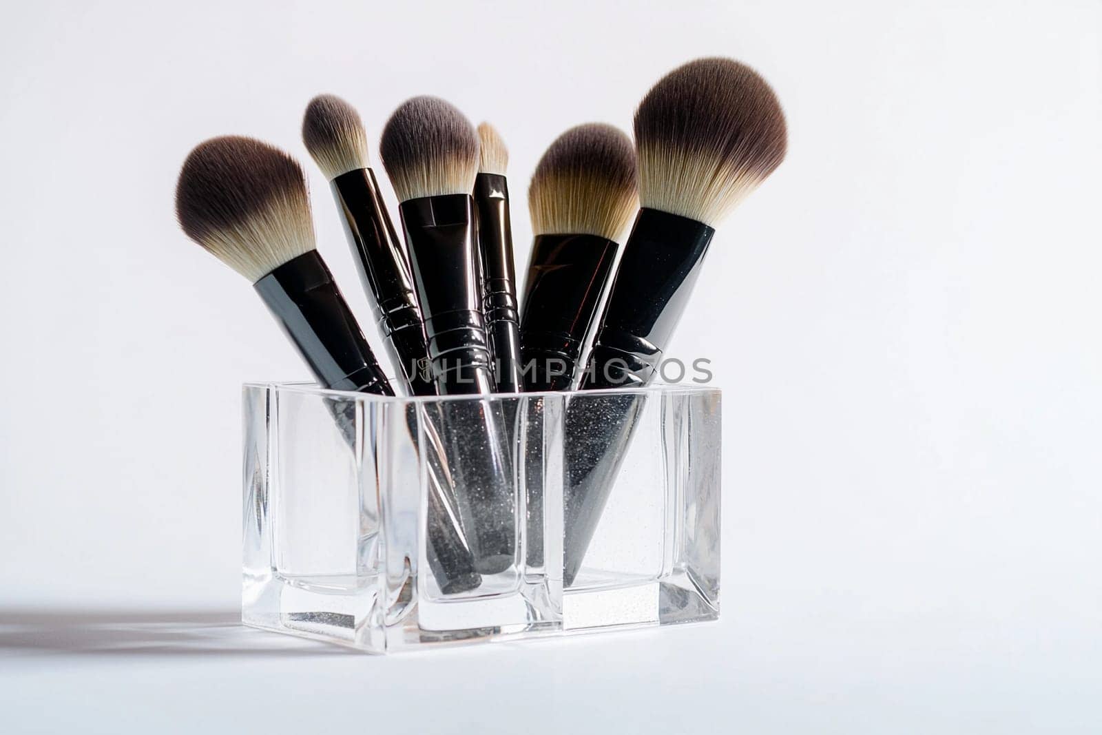 Various makeup brushes stand upright in a clear holder against a simple white backdrop.