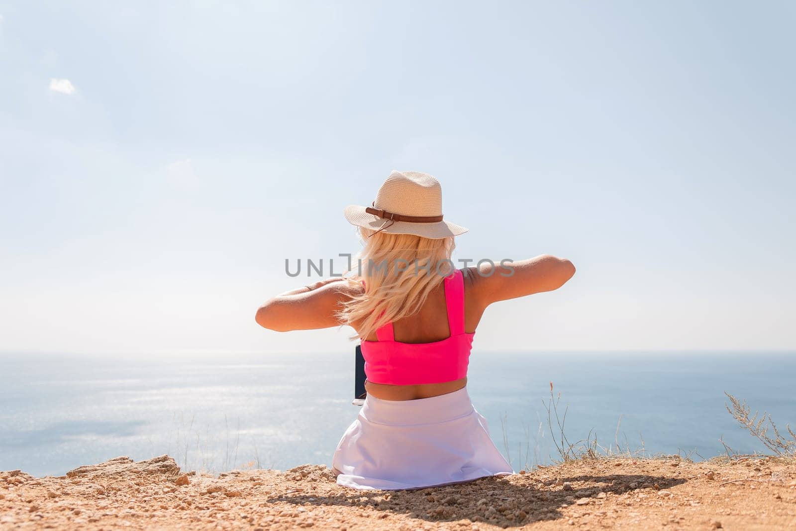 A woman in a pink top and straw hat is sitting on a beach, looking out at the ocean