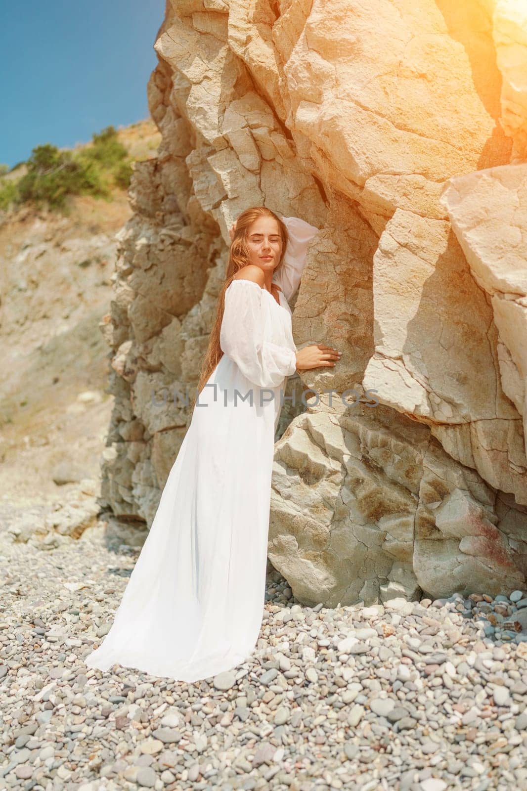 A woman in a white dress is standing on a rocky beach. Concept of serenity and tranquility, as the woman is enjoying the natural beauty of the beach