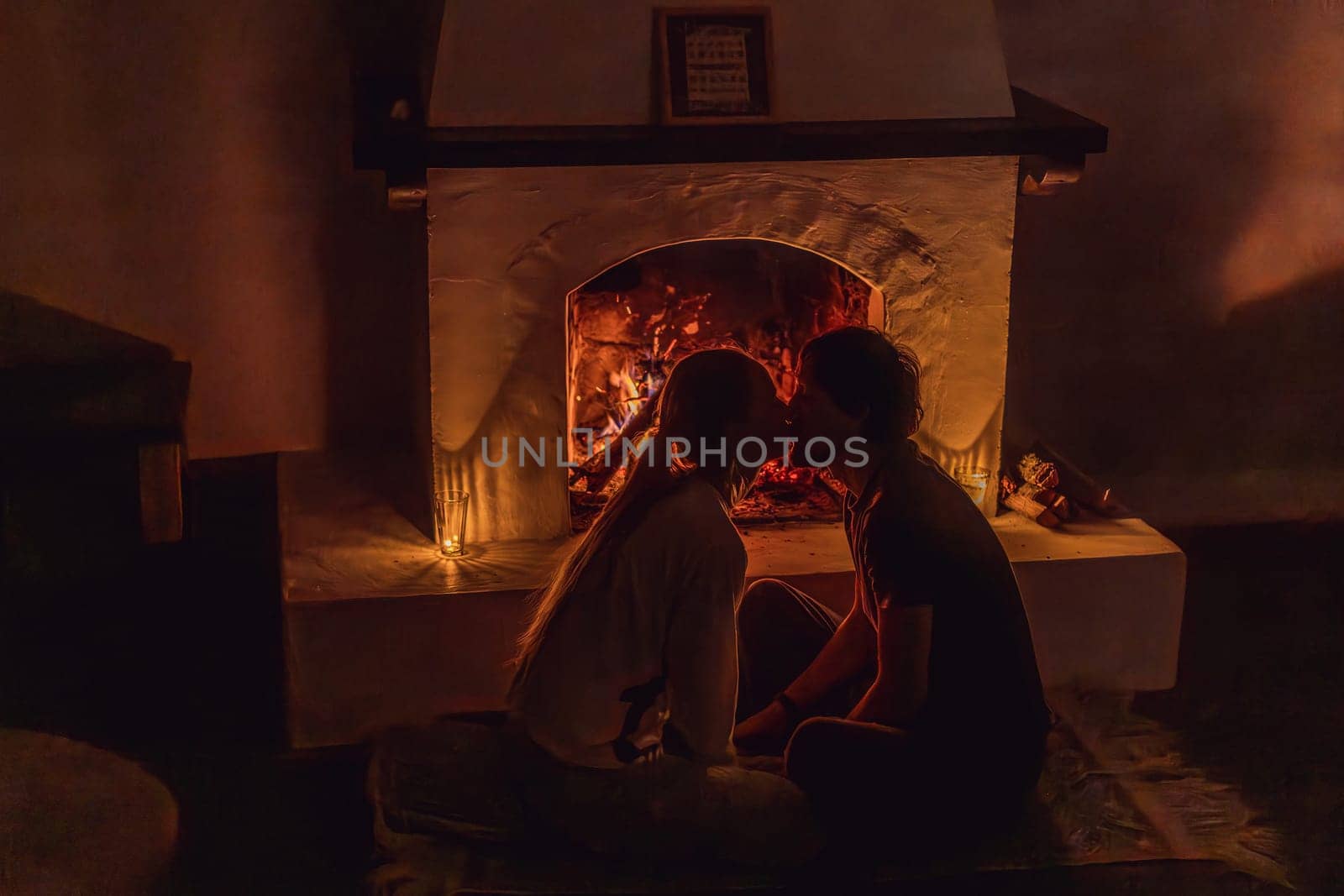 Family bonding by the fireplace during cozy winter evening. Warm and peaceful family moment indoors. Togetherness, love, and relaxation concept. A warm and inviting scene featuring a lit fireplace with glowing firewood and candles. A colorful traditional rug and pillow lie on the floor, creating a cozy atmosphere. Home, relaxation, and rustic comfort concept.
